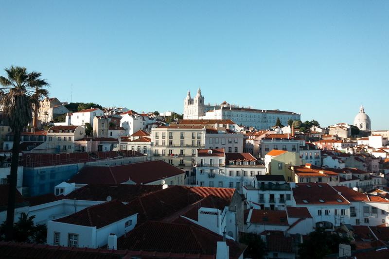 View from a rooftop in Lisbon overlooking the city on a sunny day with a bright blue sky.