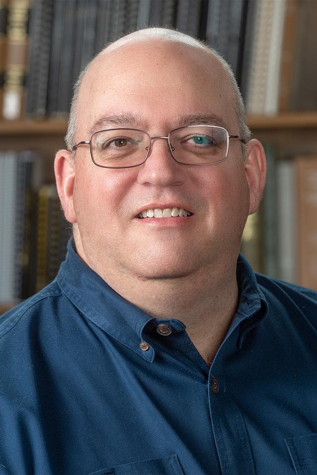 Picture of Steve Sarrica, wearing a lovely navy blue button-down shirt and wire-frame glasses. Steve is an older white guy who is heavy-set, has very little hair, and likes cocktails.