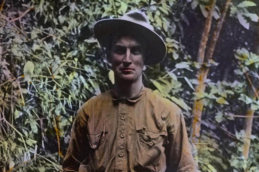 Man in a wooded setting wearing a brown shirt and a wide-brimmed hat.