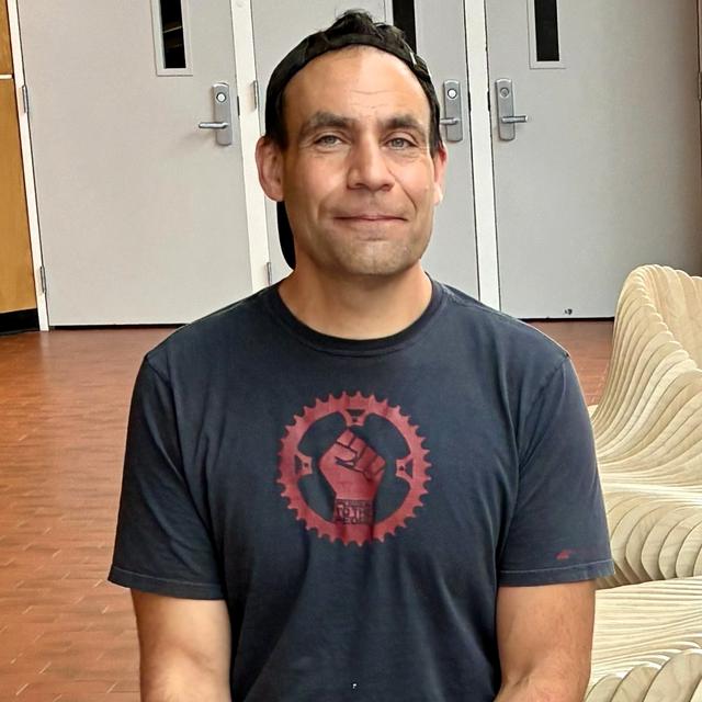 A picture of Craig from the waist up wearing a black t-shirt and a baseball hat.