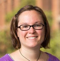 Photograph of Sarah Barbrow, a white person with short brown hair wearing clear glasses, with blurred trees in the background