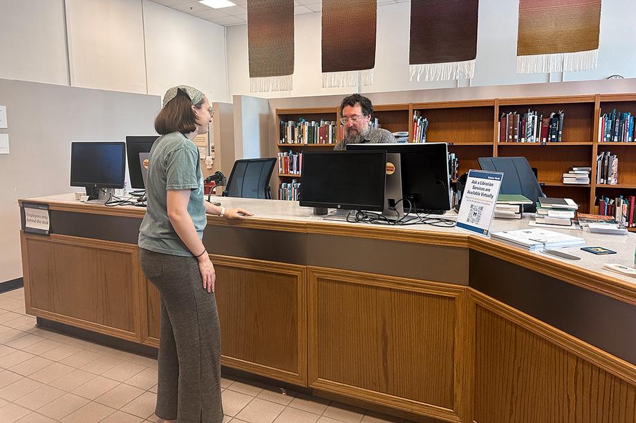 A friendly library employee helping a patron check out a book at the desk.
