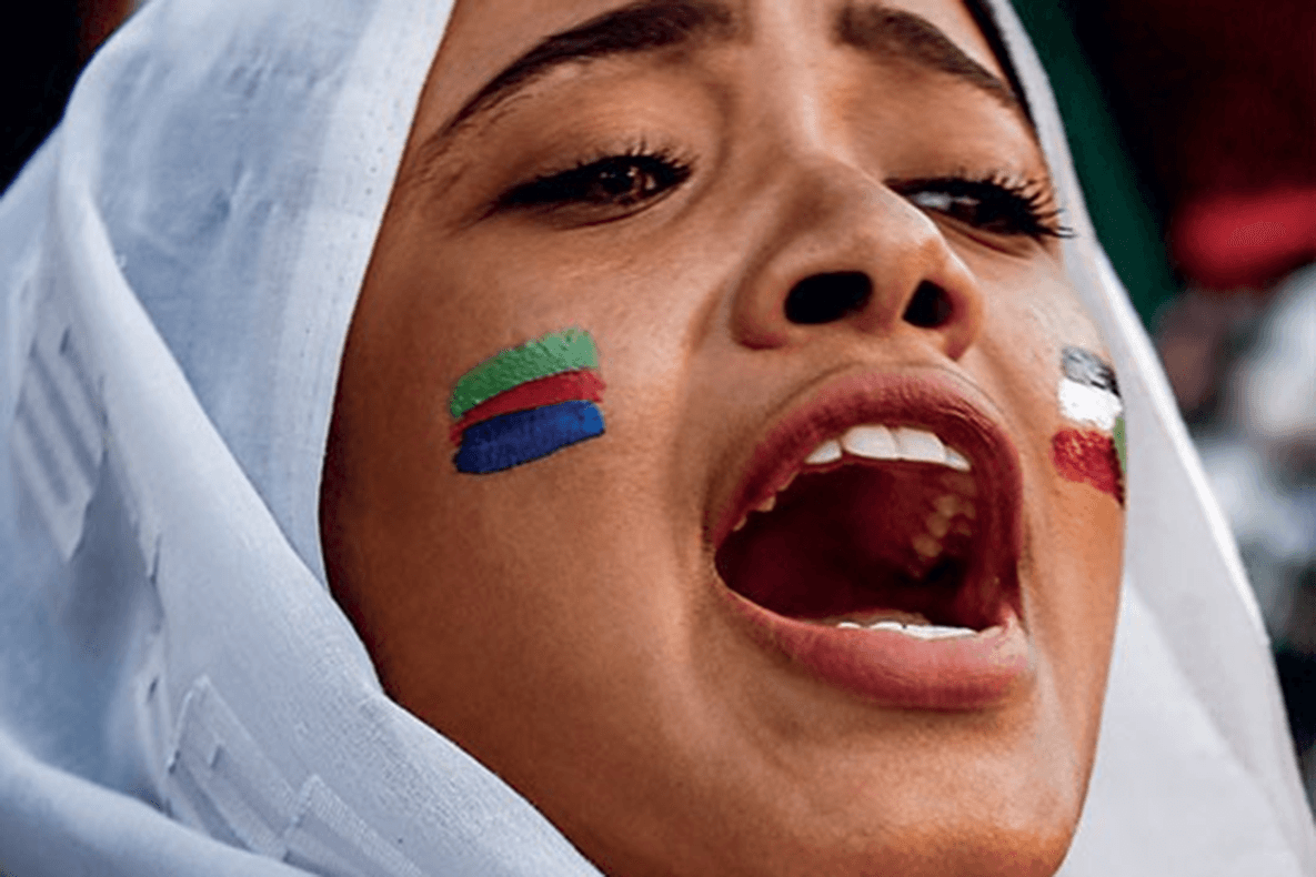 Face of a woman in a white headscarf and stripes of colors on her cheeks.