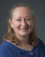 Photograph of Karen A. Reiman-Sendi, a white woman with blonde/brown hair, wearing a blue top, smiling.