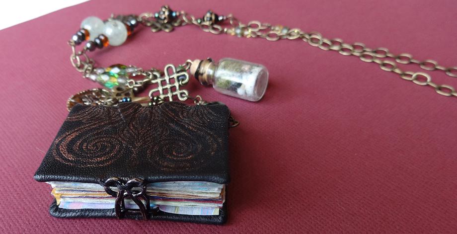 A tiny, leather-bound book with a metal clasp, attached to a necklace chain.