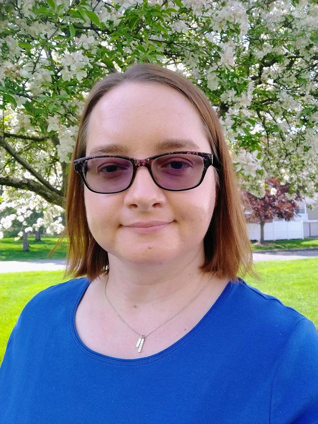 A white woman with glasses and shoulder-length brown hair, wearing a blue shirt.