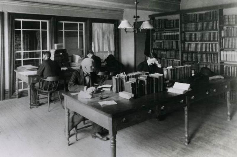 Black and white photograph of a librarian and sociology faculty member seated at tables in the library in 1890.