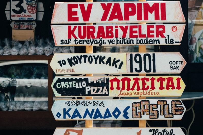 Stack of seven signs with a variety of messages written in Greek painted on them.