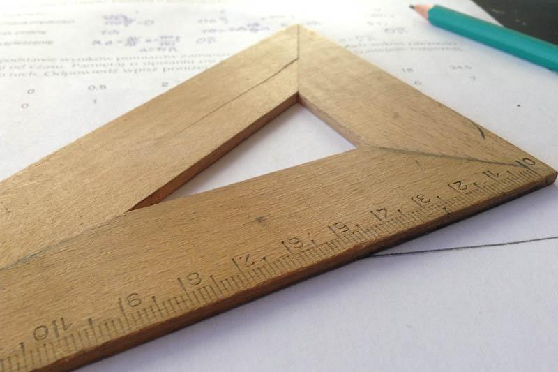 Brown wooden triangle ruler laying on top of a paper with math problems.
