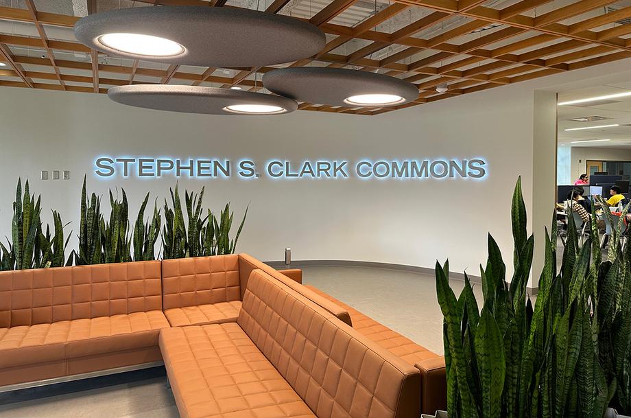 Stephen S. Clark Commons sign, with a couch and plants in the foreground.