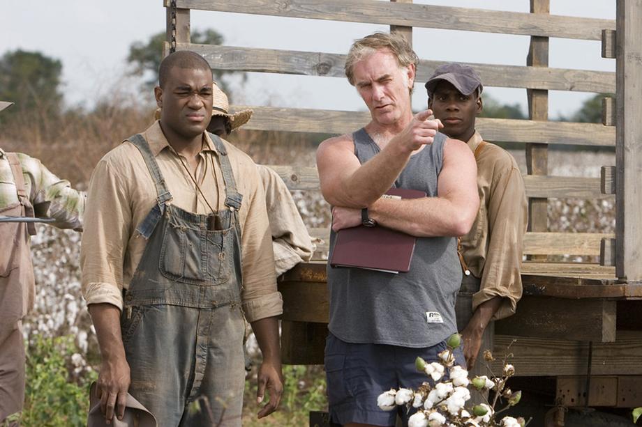 men in overalls standing in a cotton field and a director pointing with his finger