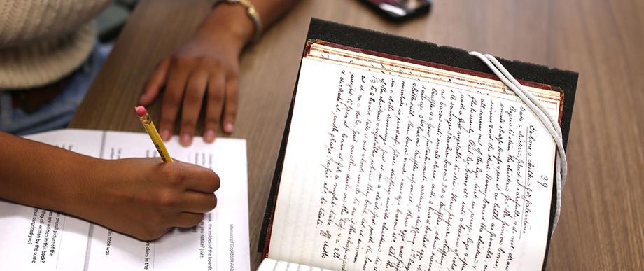 Hands of a student taking notes from a handwritten recipe book.