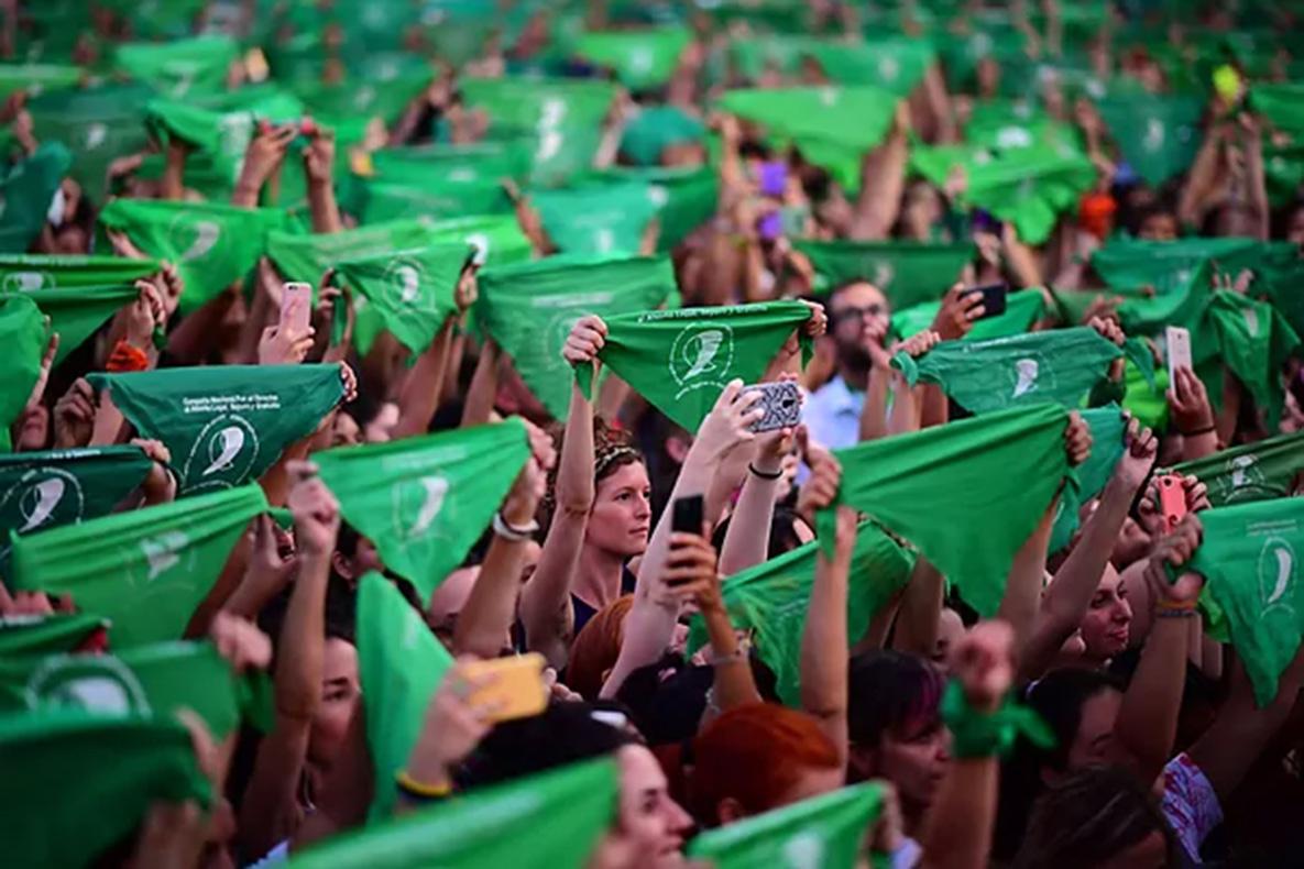 Women hold up green fabric saying abortion is legal.