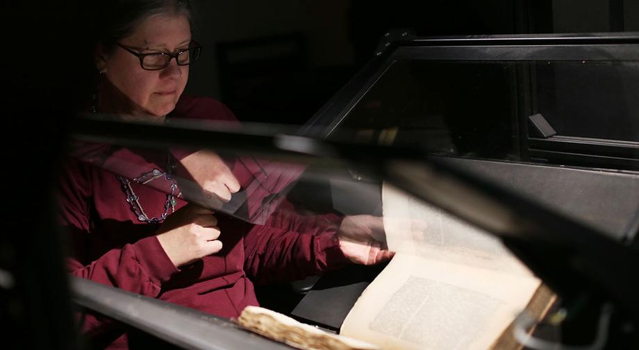 Margaret Israel turning the page of a book under the glass plate of a book scanner.