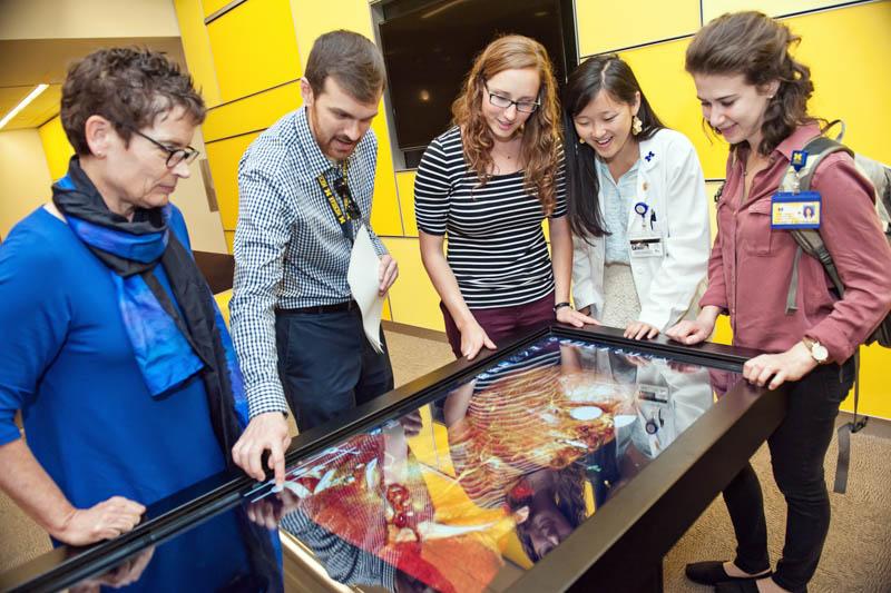 A group of five people standing around the anatomage table looking engaged.