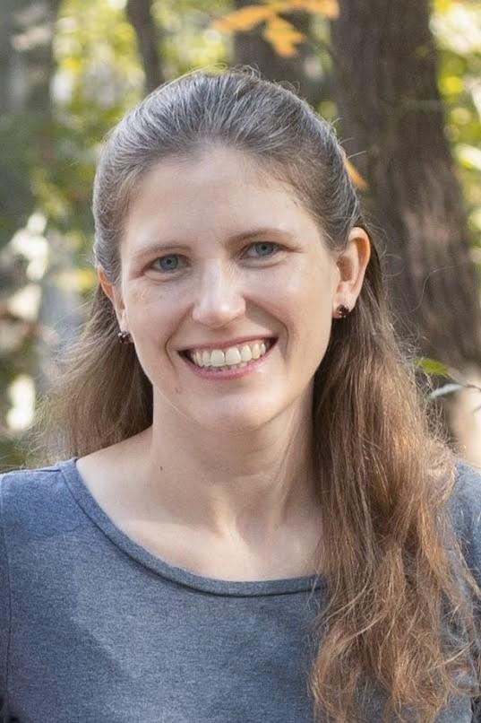 Photograph of Juli McLoone, a white woman with dark blonde hair, wearing gray.