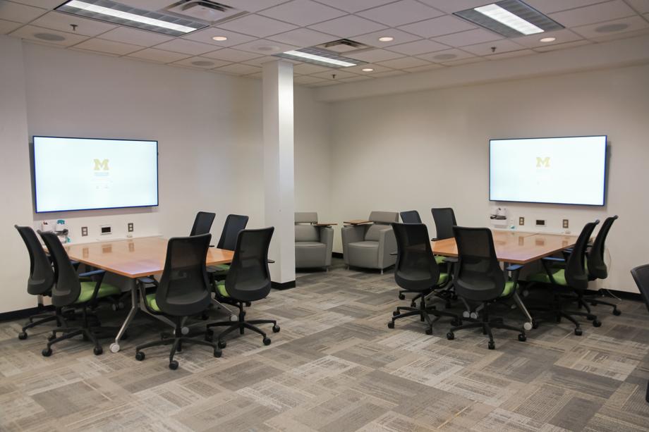 One corner of ScholarSpace, featuring 2 table pods, each with 5 chairs and a screen mounted on the wall.