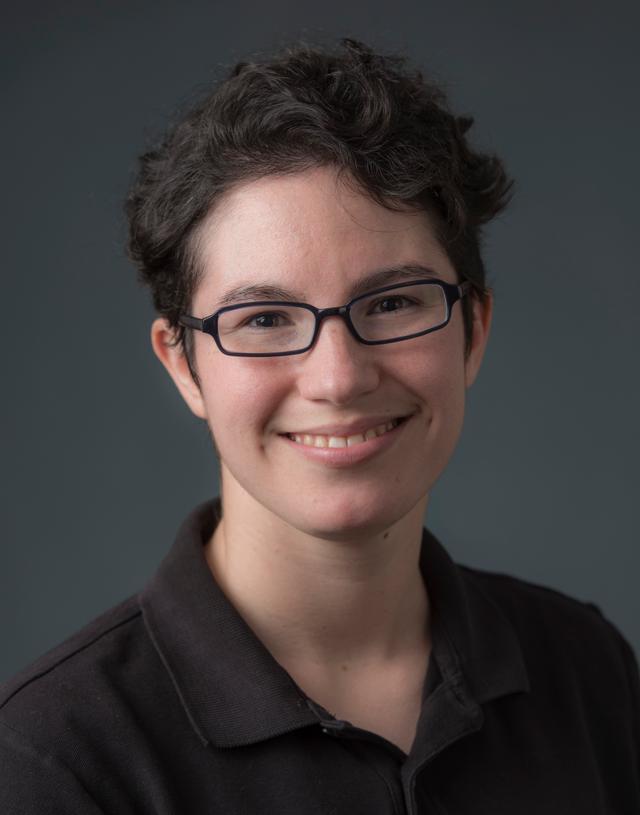 Photograph of Alica Smith, a smiling white woman with short wavy black hair, wearing a black polo shirt and glasses with a black frame.