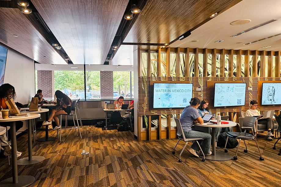 Students studying at high and low tables with windows in the background.
