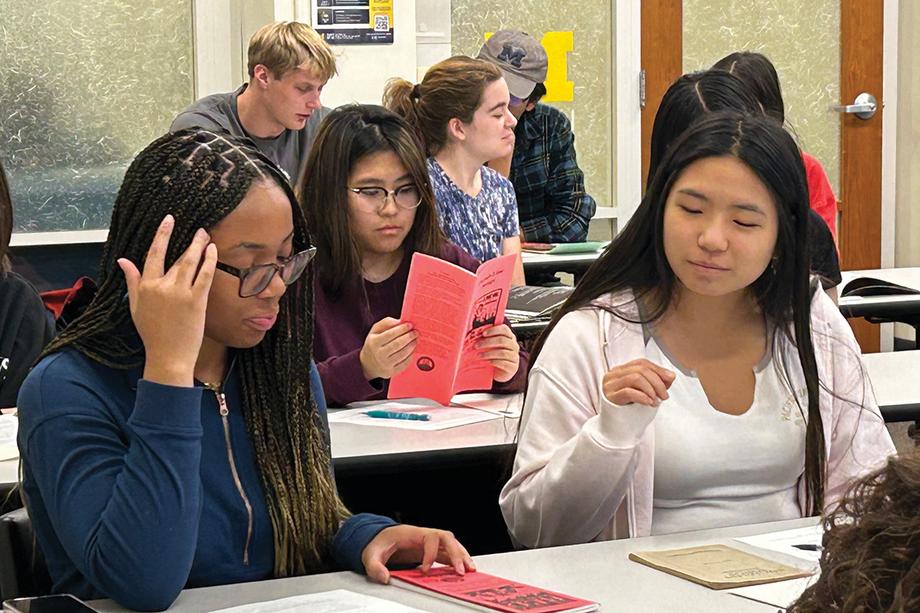 Students seated behind long tables, each looking at a different pamphlet or musical score.