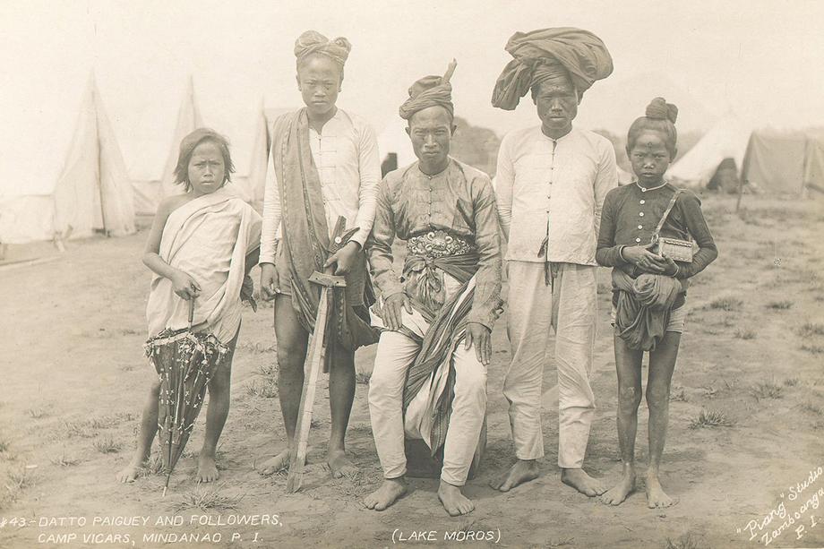 Photograph of Datto Paiguey seated with 2 people standing on either side