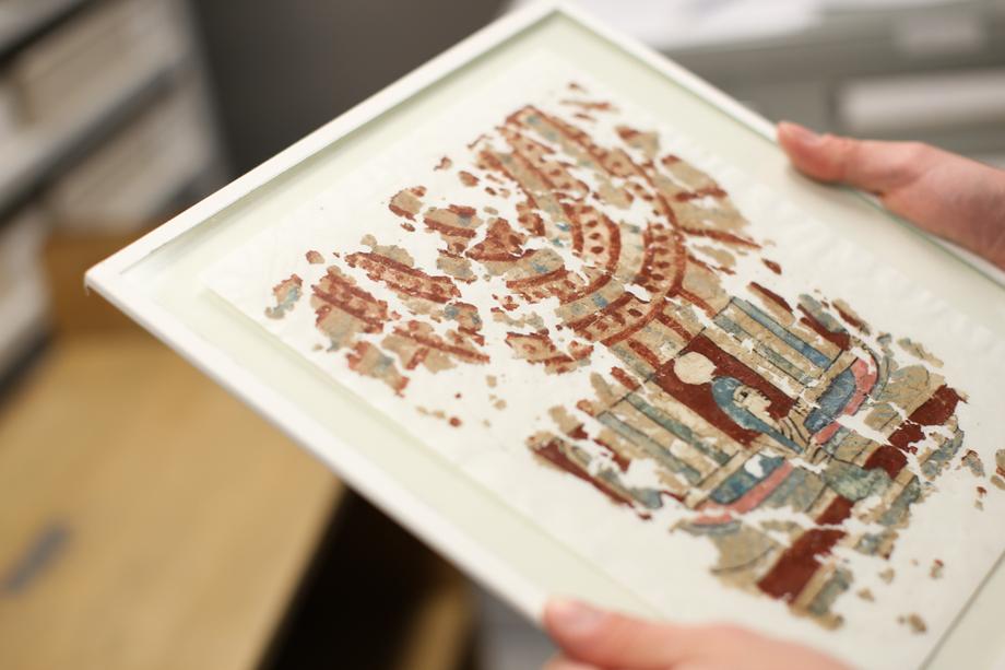 Close up of hands holding framed papyri with a colorful painting of a pharaoh. 