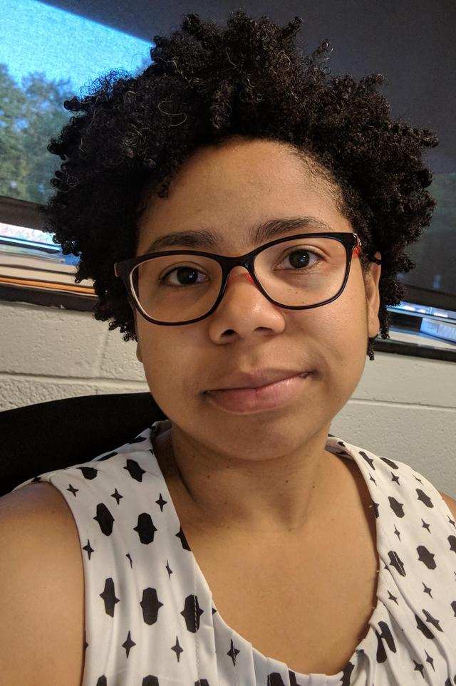 African-american woman facing camera wearing glasses and a white and black top.