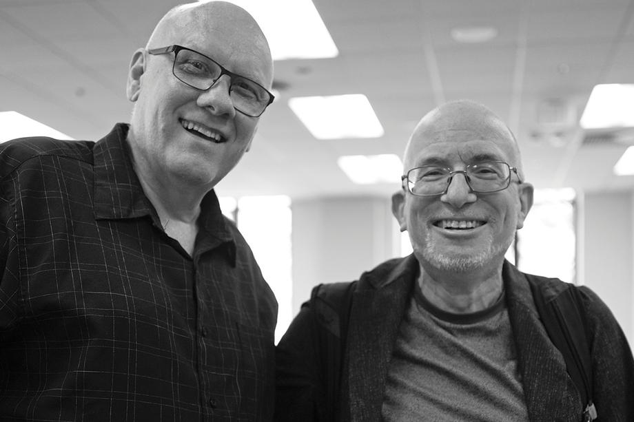 Two bald men, both wearing glasses, and smiling into the camera.