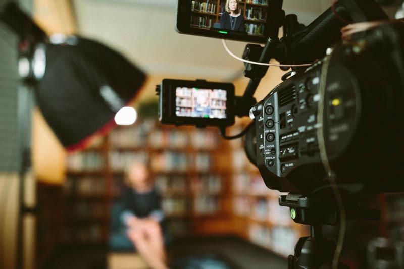 Close-up image of a video camera with a person being interviewed in the background.