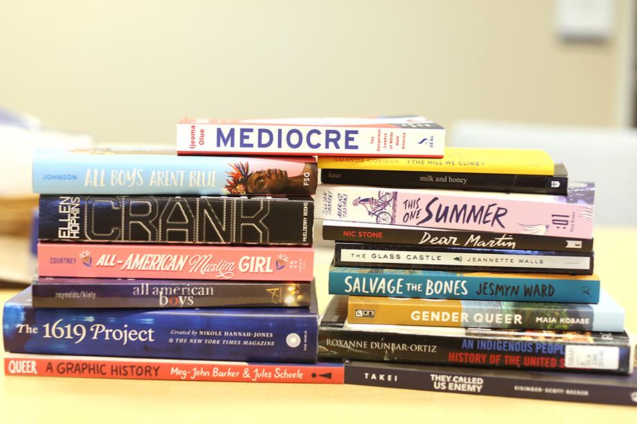 Horizontal stack showing book spines of 16 books that have been banned, including Gender Queer, Crank, and more.