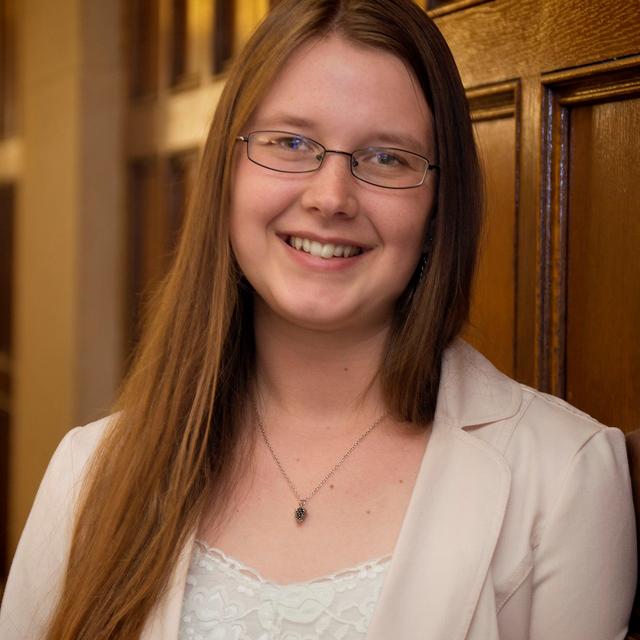 A young, white woman wearing glasses smiles warmly.